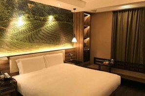 A hotel room with a large bed, a nightstand with a phone, a small table with a lamp, a wall-mounted shelf, and a window with curtains. - Yiwang Hotel Collection (Wenzhou Avenue) (Wenzhou)