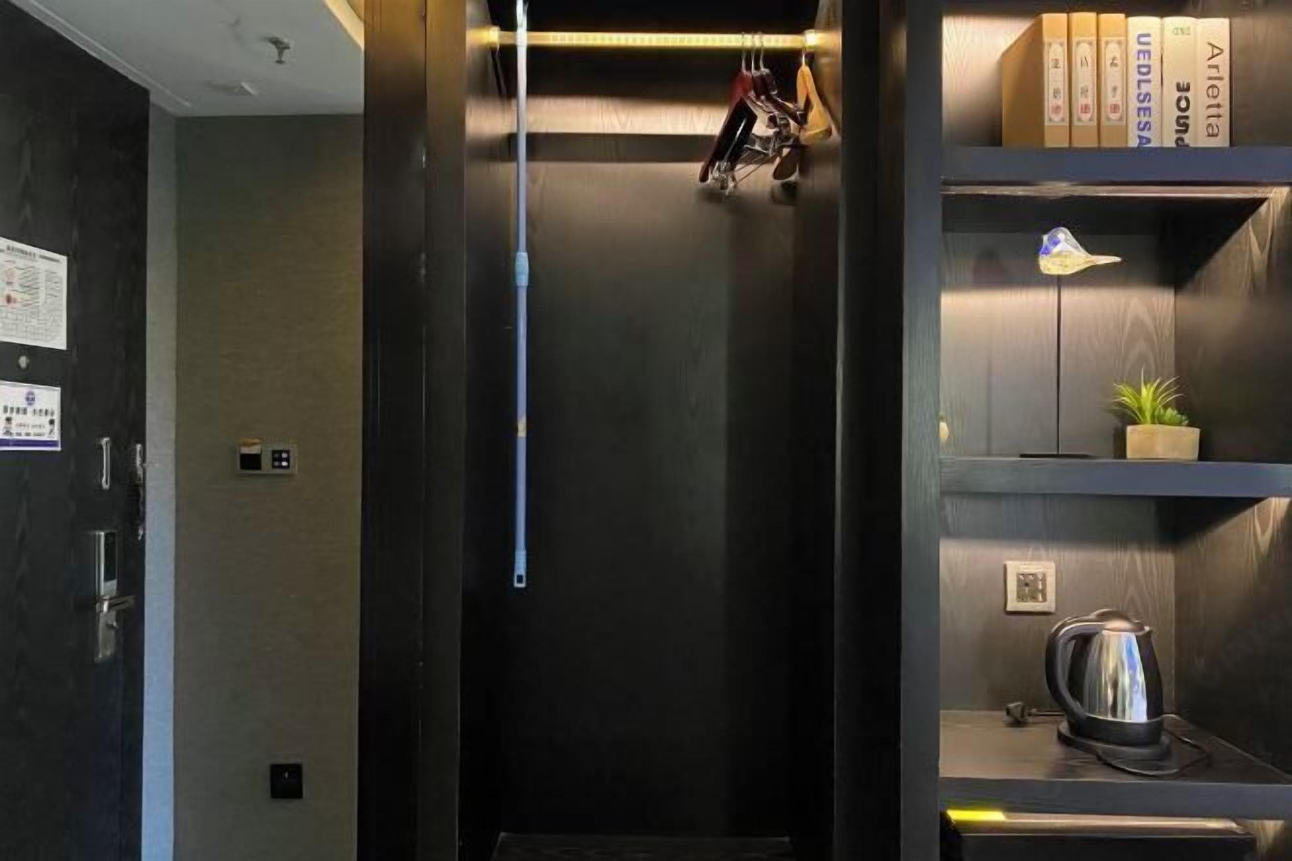 Un ascensor de hotel con interior oscuro, una pequeña planta en maceta y una tetera a la derecha.