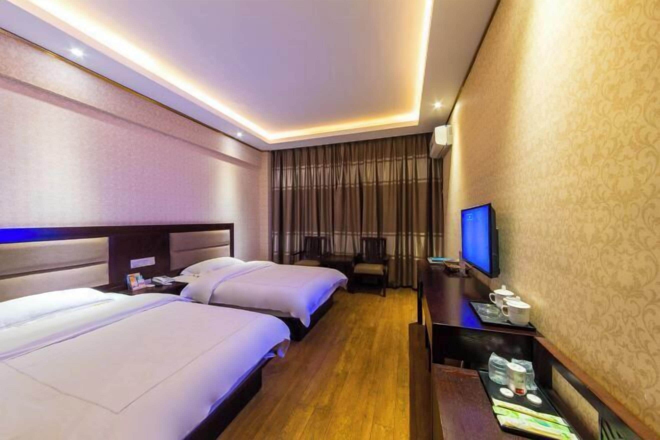 A hotel room with two beds, a desk with a flat-screen TV, and a seating area with a chair.