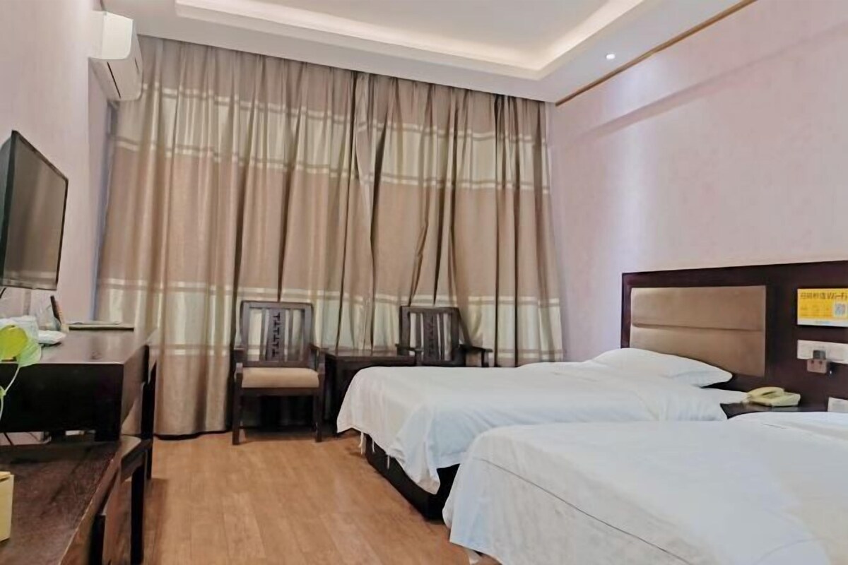 A hotel room with two beds, a desk with a chair, a television, and a window with curtains.