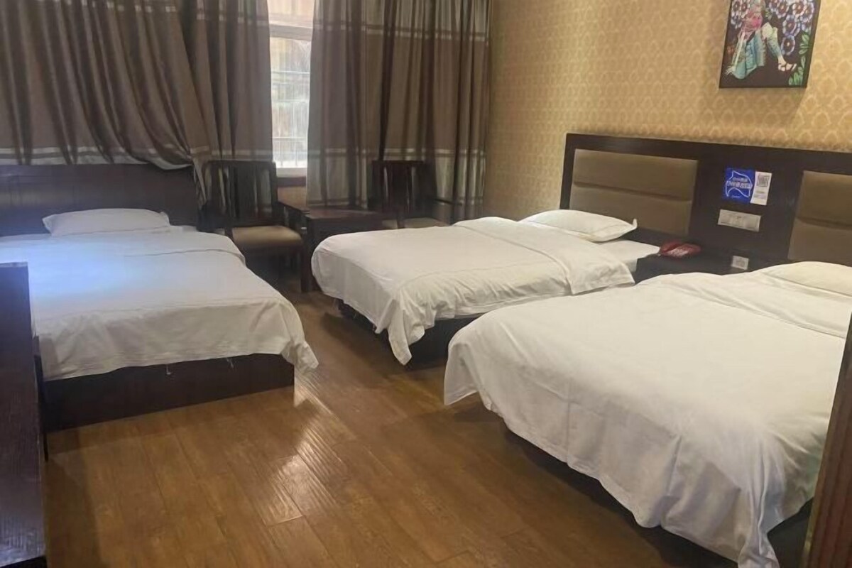 A hotel room with three beds, a wooden floor, a chair, and a window with curtains.