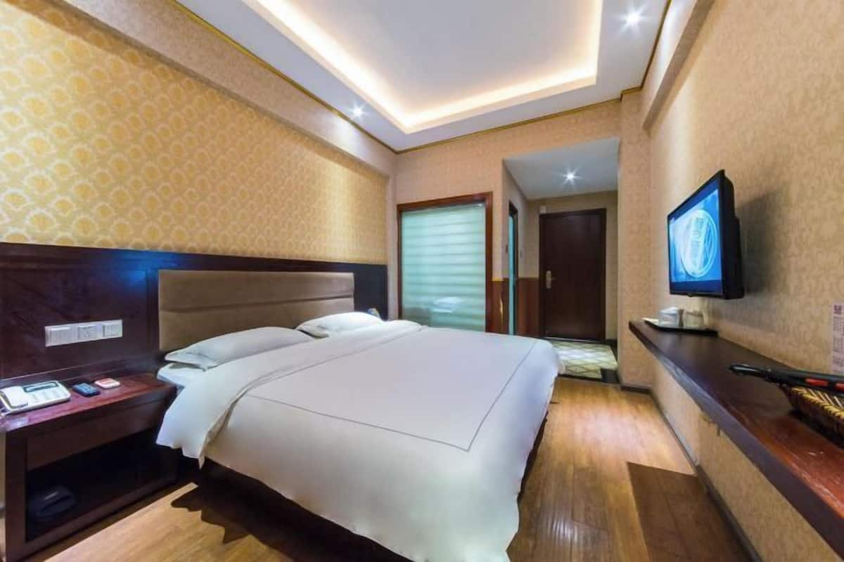 Une chambre d’hôtel comprenant un lit, une table de chevet, une télévision et un petit bureau avec une chaise.