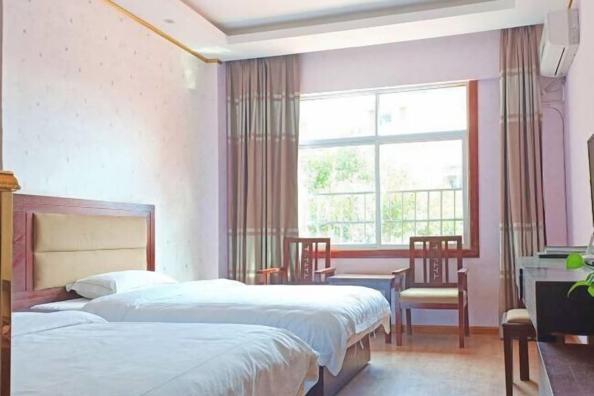 A hotel room with two beds, a desk, chairs, and a large window.