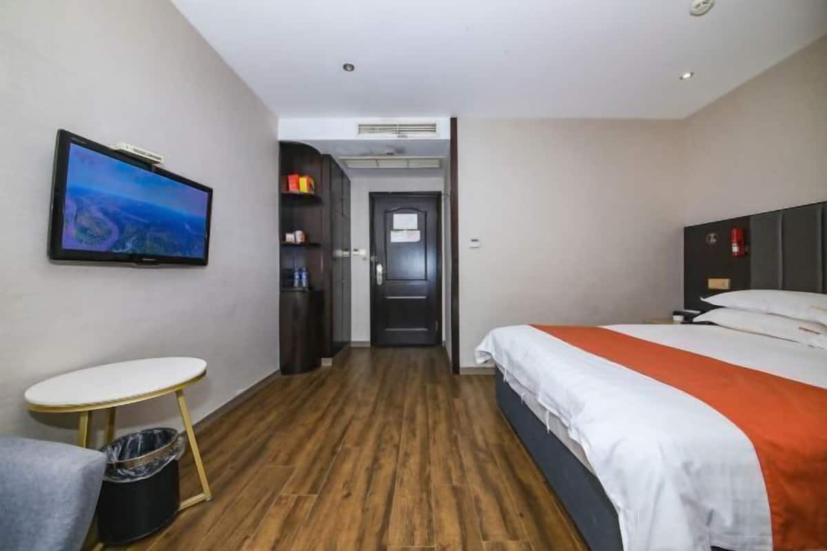 A hotel room with a bed, a TV, a small table, and a trash bin.