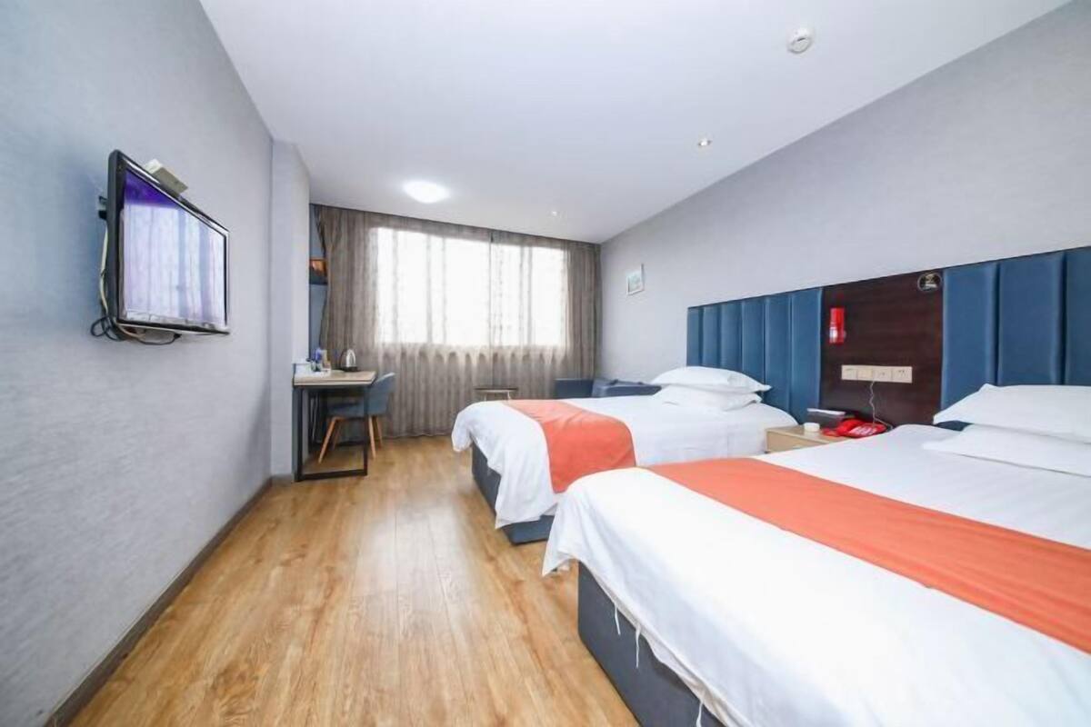 A hotel room with two beds, a desk, a television, and a window with curtains.