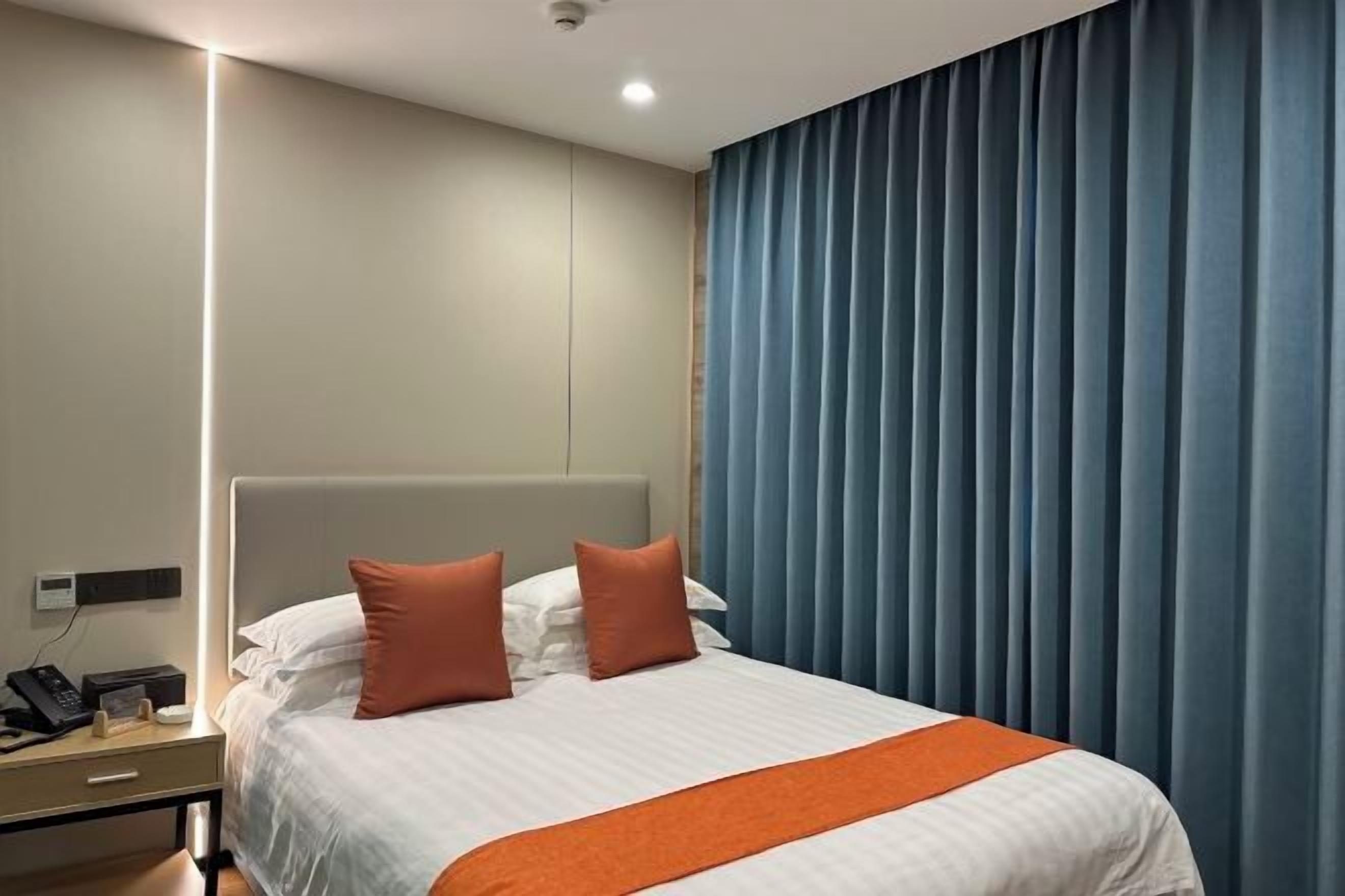Quarto de hotel com cama, mesa de cabeceira com telefone e janela com cortinas.
