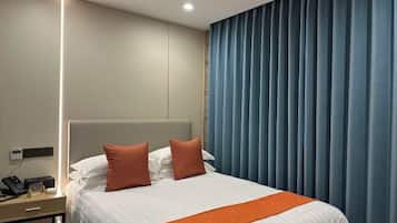 Quarto de hotel com cama, mesa de cabeceira com telefone e janela com cortinas.