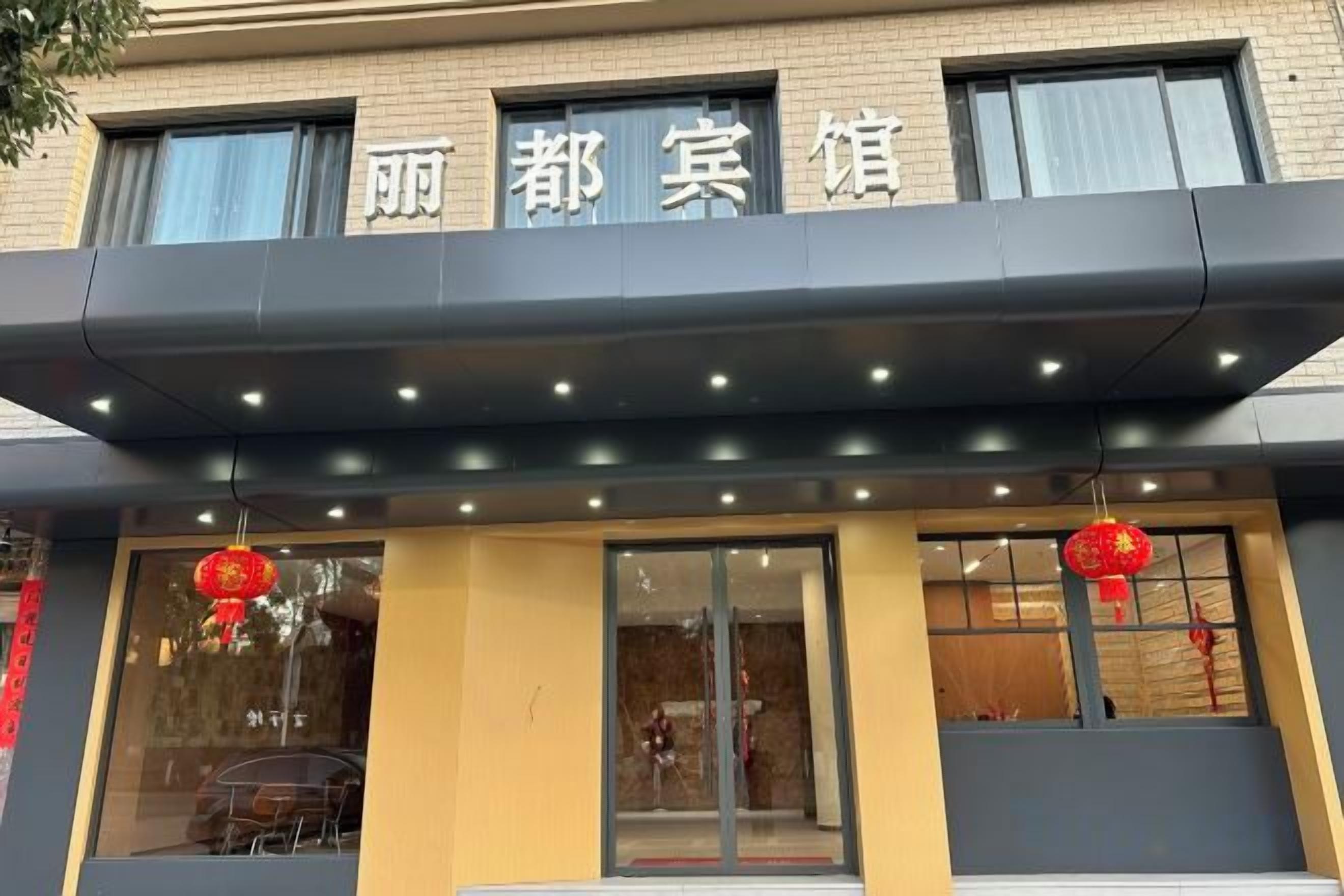 A building with a sign that reads '丽都宾馆' and a covered entrance area with lights.