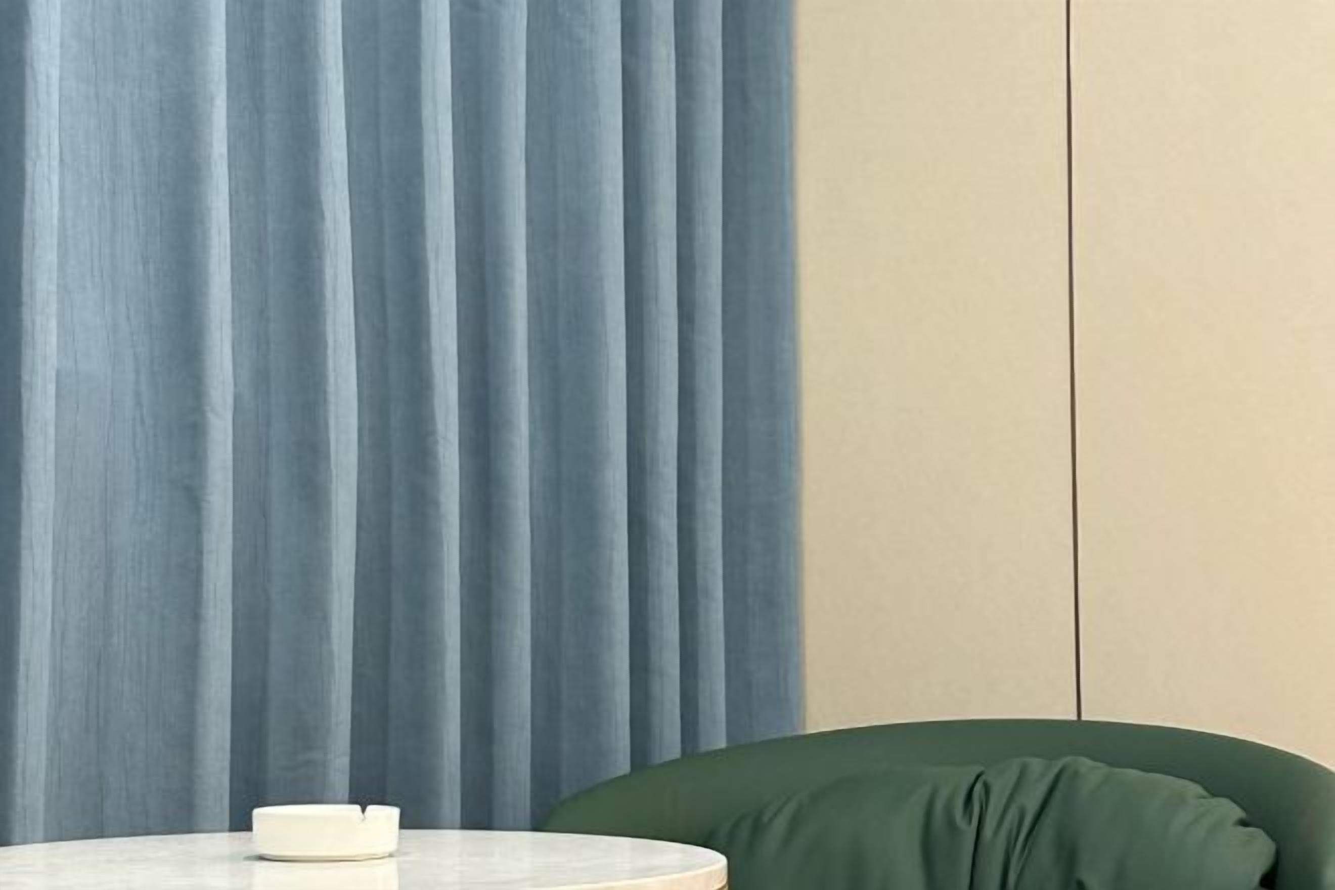 Una habitación con una cortina azul, una silla verde y una mesa blanca.