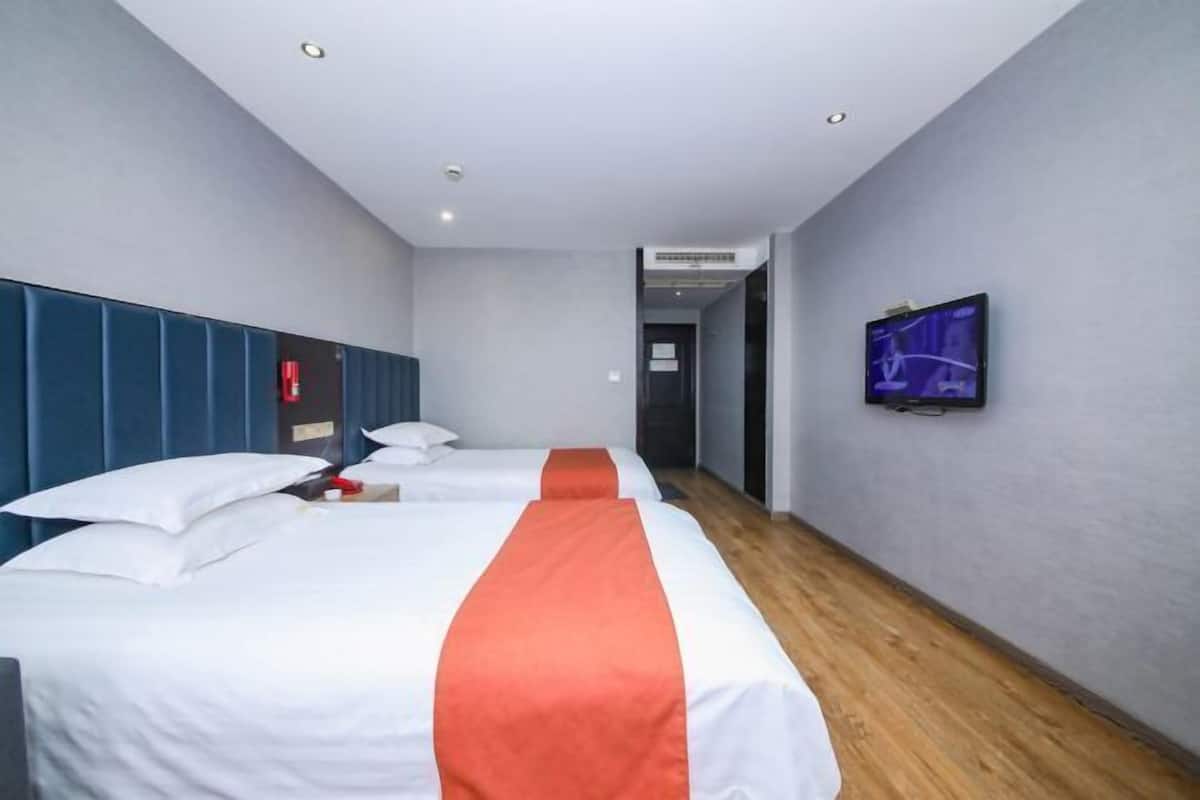 A hotel room with two beds, a TV on the wall, and a wooden floor.