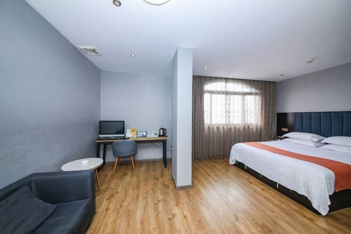 A modern hotel room with a single bed, a desk with a computer, a chair, and a small table.