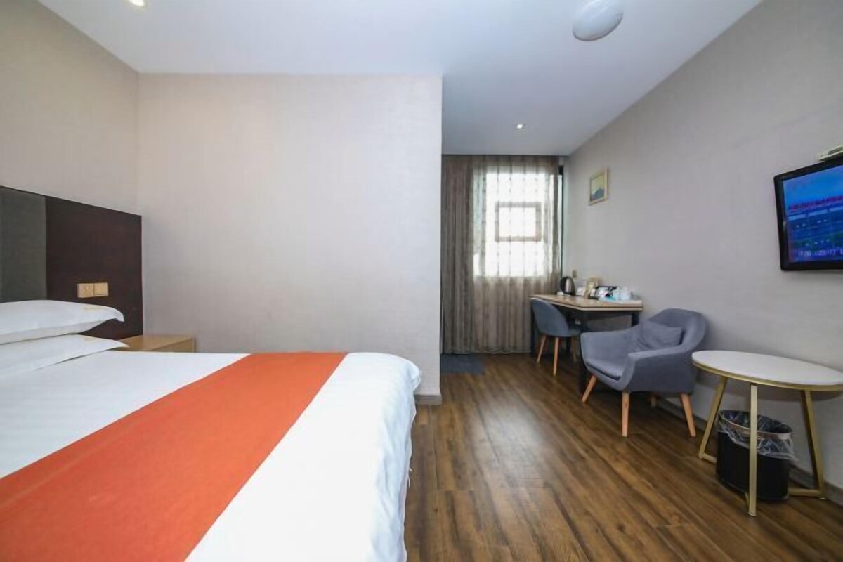 A hotel room with a bed, a desk, a chair, a small table, and a television.