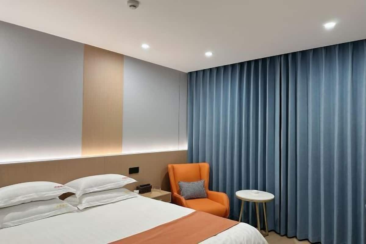 A hotel room with a bed, a chair, a small table, and a curtain.