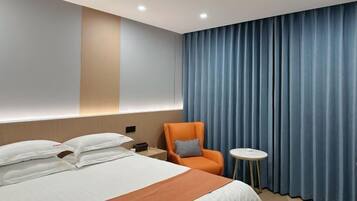 Una habitación de hotel con una cama, una silla, una mesita y una cortina.