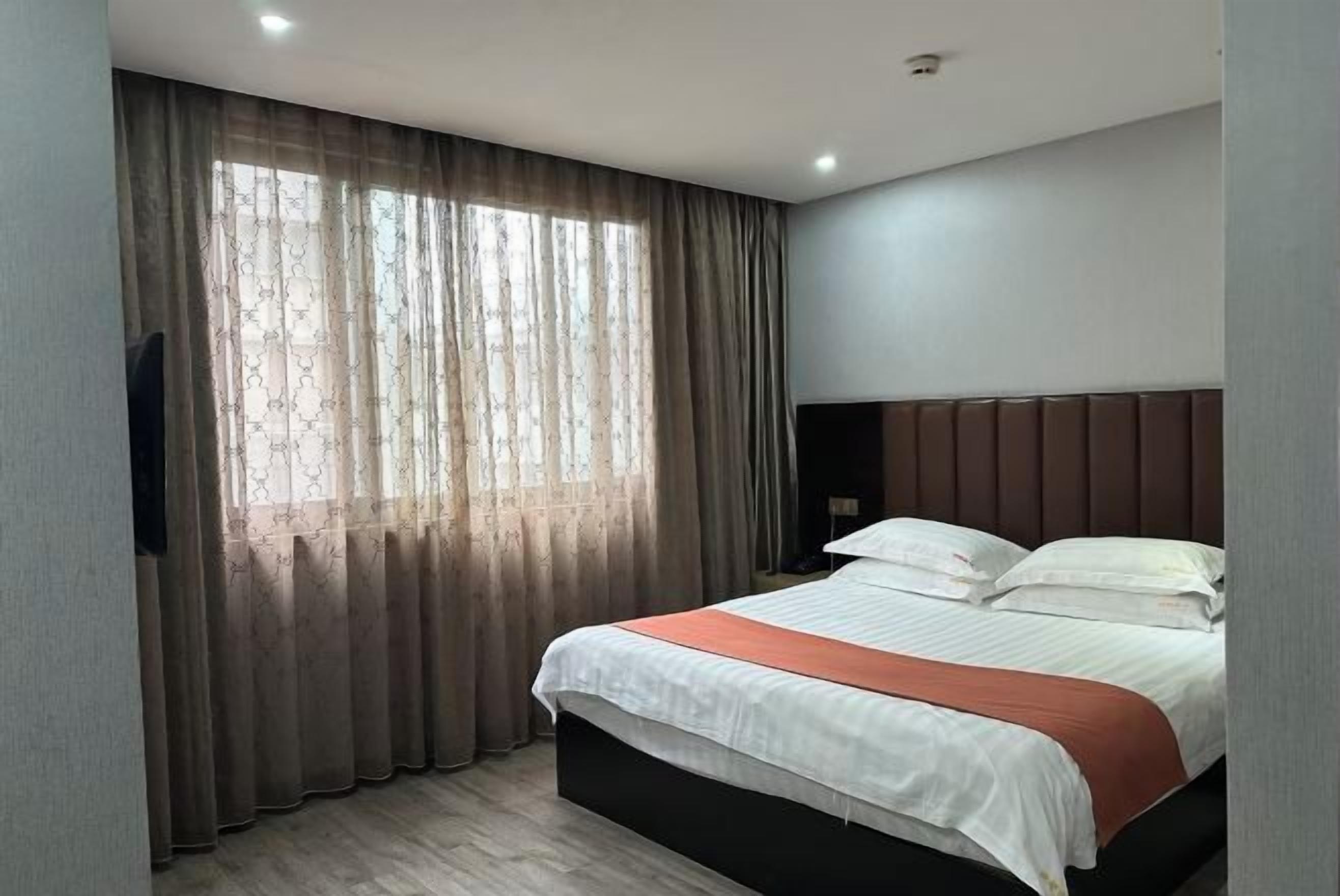 Une chambre d’hôtel avec un lit, des rideaux, une tête de lit et un téléviseur fixé au mur.