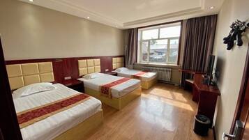 A hotel room with three beds, a desk, a chair, a radiator, and a window with curtains.