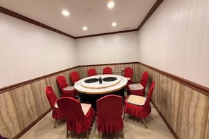A conference room with a round table and red chairs, white walls, and a wooden floor.