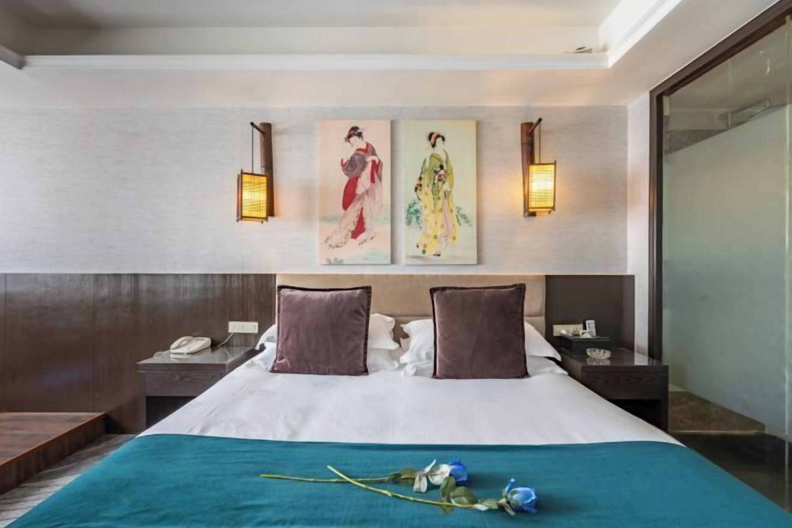 A hotel room with a large bed, two wall-mounted lamps, and artwork above the bed.