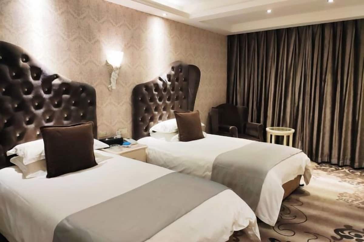 Une chambre d’hôtel avec deux lits, une table de chevet, une chaise et un rideau.