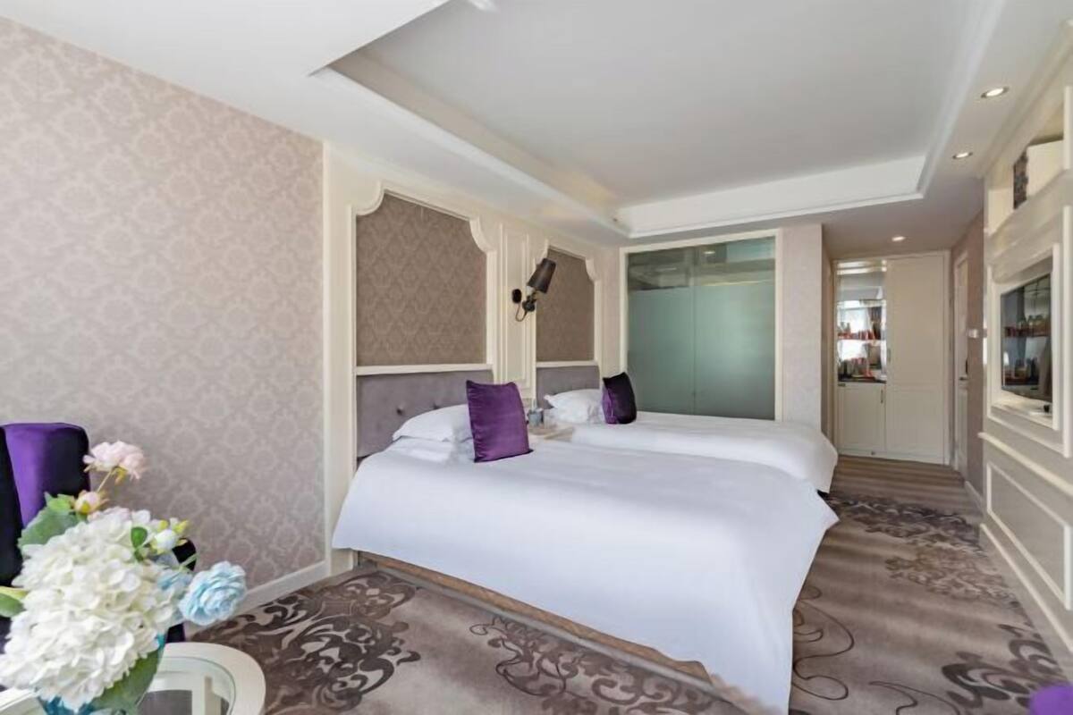 Een hotelkamer met twee bedden, een grote spiegel, een decoratieve vaas met bloemen en een kamerbreed tapijt met dessin.