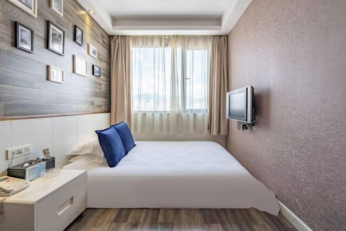 Une chambre d’hôtel avec un lit, une table de chevet, une télévision et une fenêtre avec des rideaux.