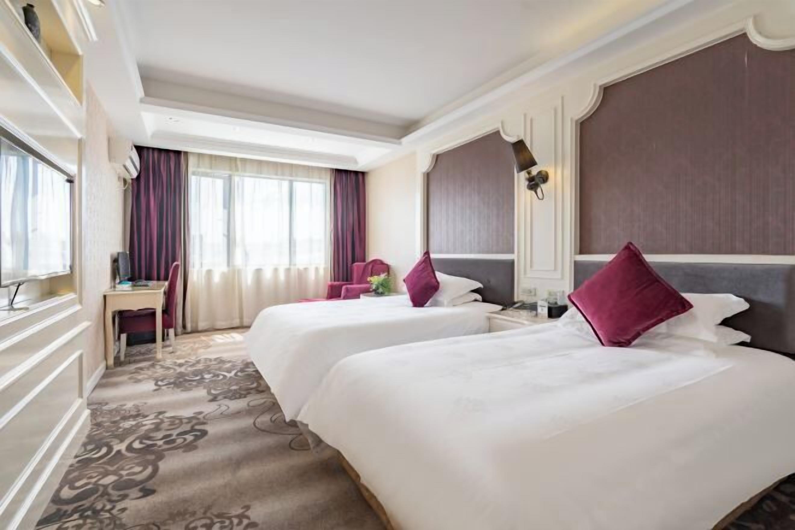A hotel room with two beds, a desk, and a chair.