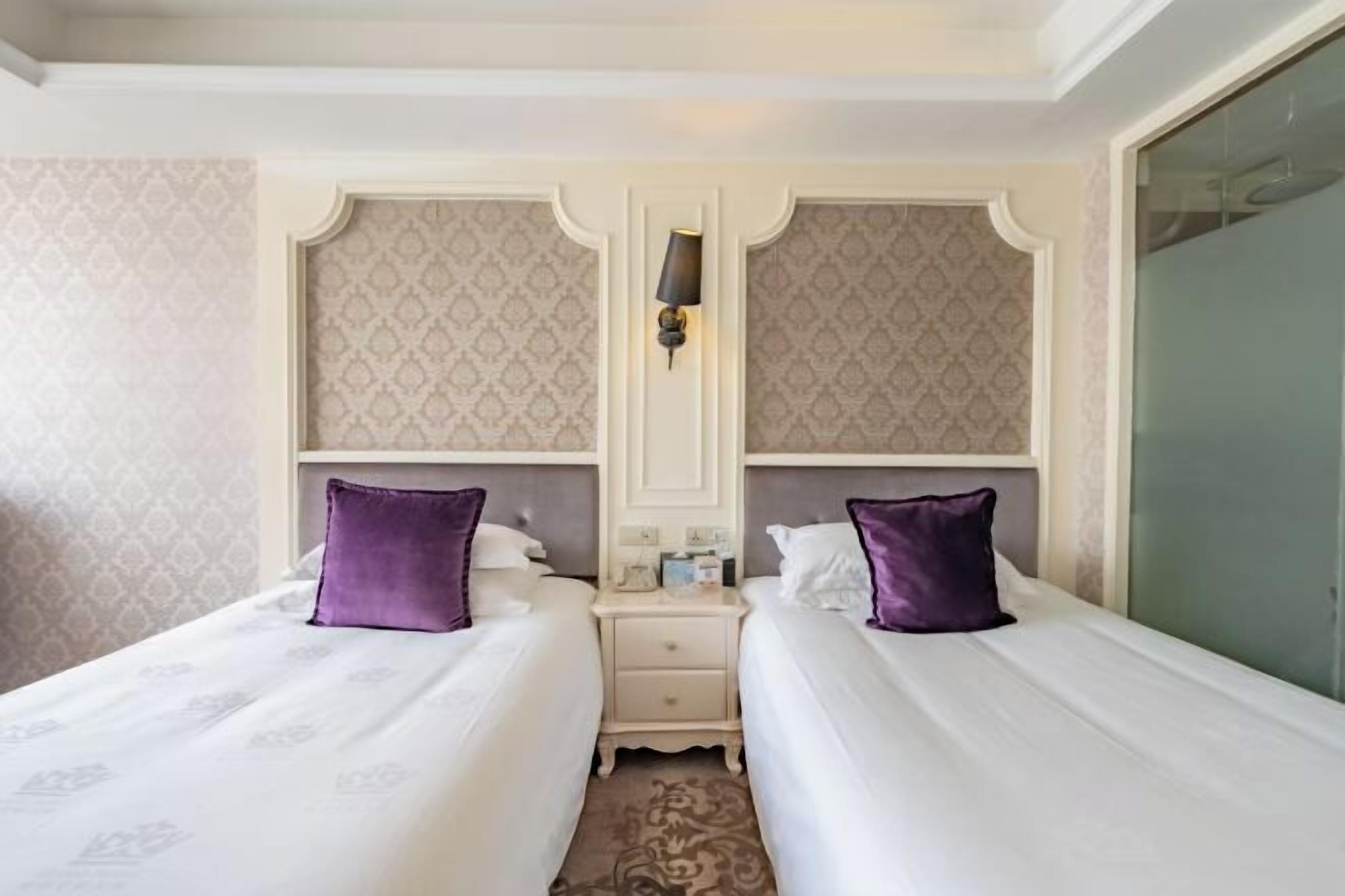 A hotel room with two beds, a nightstand, a lamp, and a mirror.