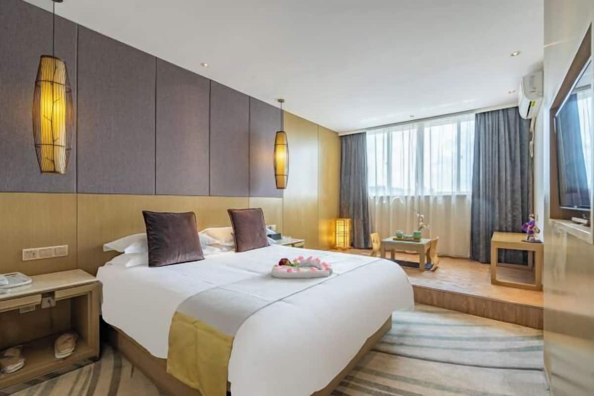 Une chambre d’hôtel avec un grand lit, des tables de chevet, un bureau, une chaise, une télévision et une fenêtre avec des rideaux.