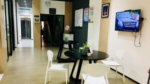 A modern office space with a reception desk, a black round table with chairs, and a mounted television displaying a car. - Gelin Luoman Fengqing Hotel (Lishui)