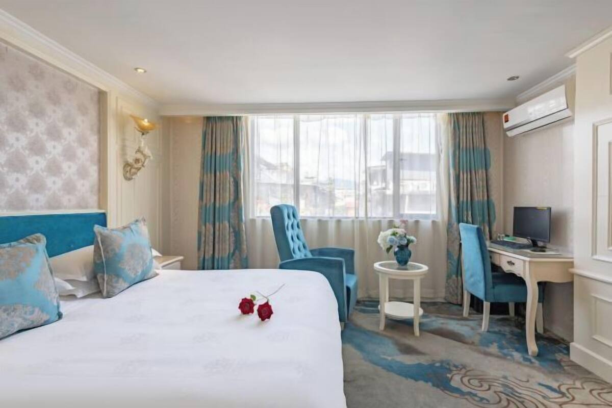 Une chambre d’hôtel comprenant un lit, un bureau, une chaise, une petite table avec un vase et un appareil de climatisation.