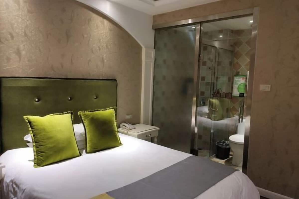 Une chambre d’hôtel comprenant un lit, une table de chevet, une salle de bain avec une douche à parois de verre et des toilettes.