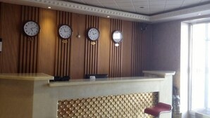 A reception desk with clocks, a patterned wall, and a window. - Xiaohonglou Hotel, Luohe (Nehe)