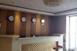A reception desk with clocks, a patterned wall, and a window. - Xiaohonglou Hotel, Luohe (Nehe)