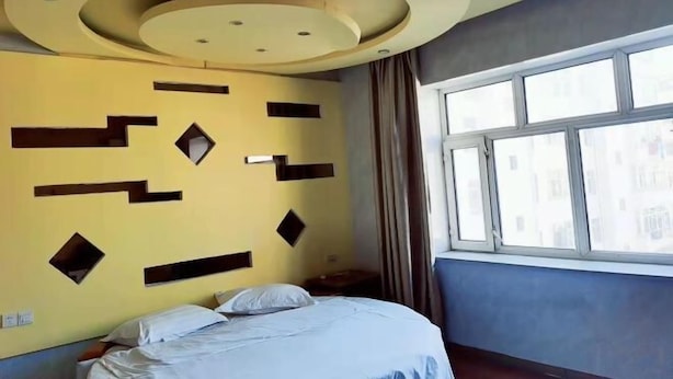 A hotel room with a bed, a window with curtains, and a unique ceiling design. - Xiaohonglou Hotel, Luohe (Nehe)
