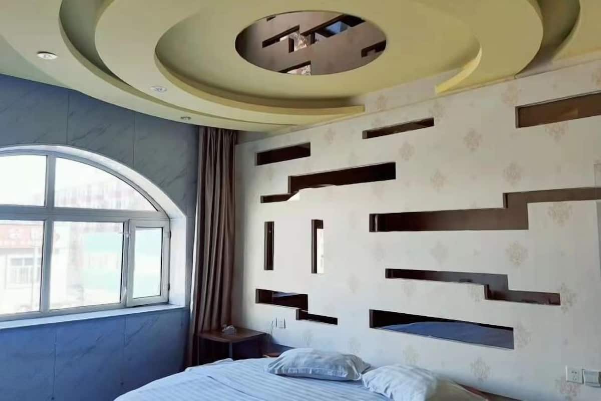 Habitación de hotel moderna con techo curvo, ventana grande y cama con cabecera que incorpora estantes.