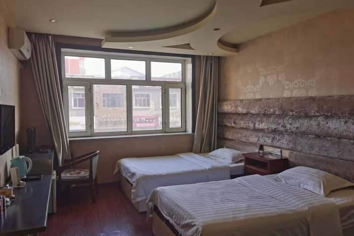 Habitación de hotel con dos camas, un escritorio con silla, ventana con cortinas y pared de piedra.