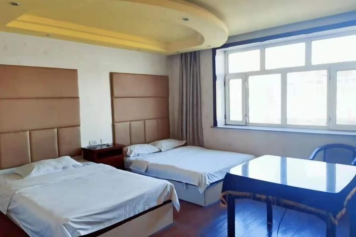 Una habitación de hotel con dos camas, una mesita y un ventanal.