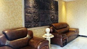 A room with two leather sofas, a decorative wall with relief sculptures, and a patterned wallpaper. - Xiaohonglou Hotel, Luohe (Nehe)