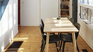 A dining area with a wooden table and chairs, a ceiling fan, a bookshelf, and a staircase with blue railings.