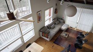 A spacious living area with a wooden floor, a grey sofa, a coffee table, and a dining table.
