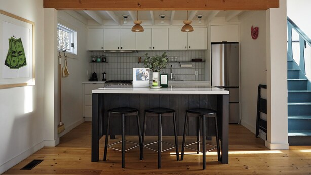 A modern kitchen with white cabinets, a wooden ceiling, and a central island with stools.