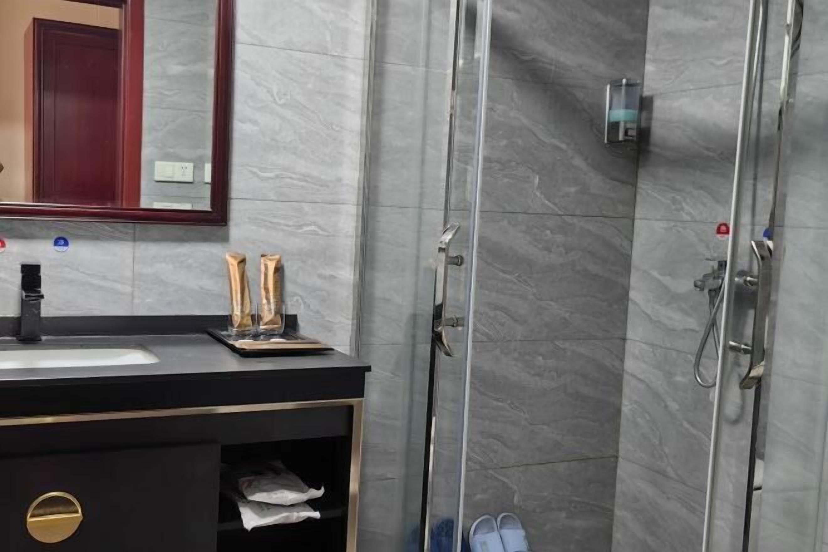Une salle de bain moderne dotée d’une douche à parois de verre, d’un meuble-lavabo noir agrémenté de détails dor és et d’un mur recouvert de carreaux de marbre.