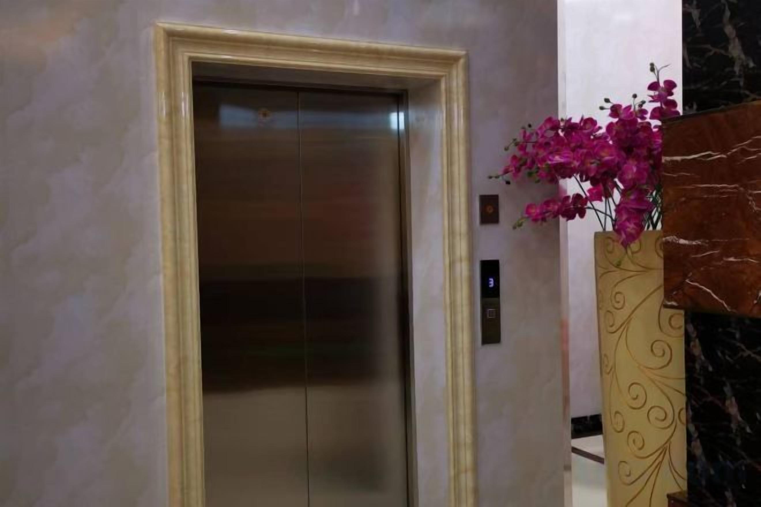 An elevator with a marble wall and a decorative vase with flowers.