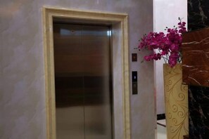 Un ascenseur avec un mur en marbre et un vase décoratif rempli de fleurs.