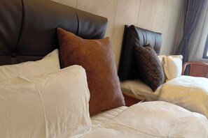 Una cama con almohadas blancas y marrones, un cabecero oscuro y una ventana con cortinas.