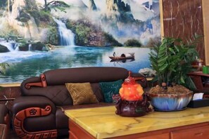 A room with a sofa, a table with a lamp, a potted plant, and a painting of a waterfall.