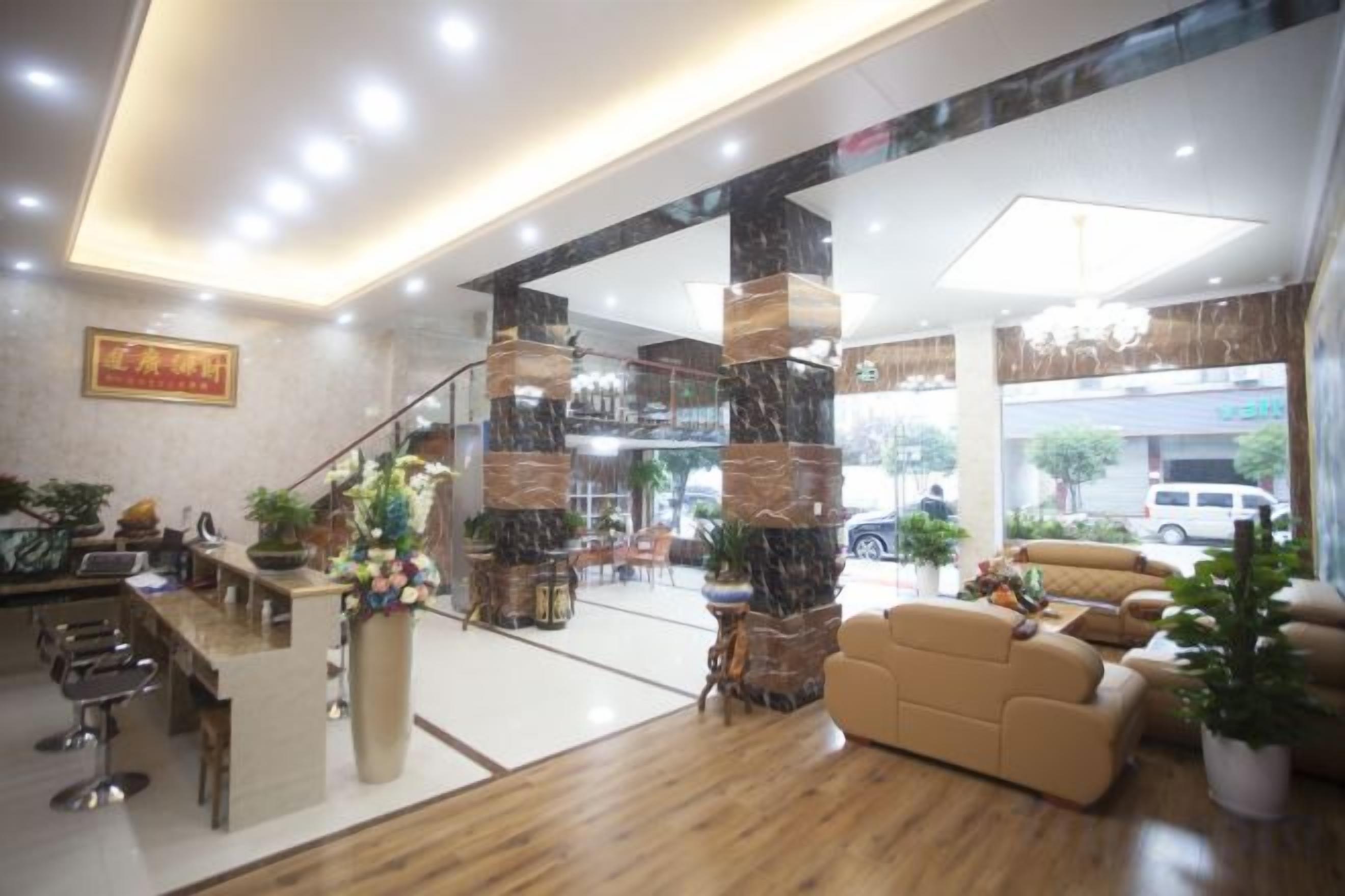 A hotel lobby with a reception desk, seating area, staircase, and large windows.