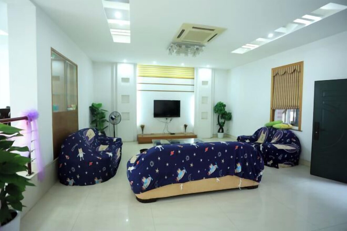 Una sala moderna con un televisor de pantalla plana, dos sillones tipo puffs, una mesa de centro y un espejo grande.