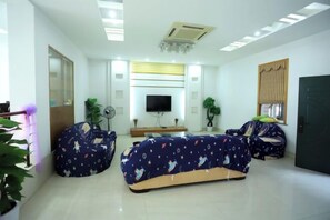 Una sala moderna con un televisor de pantalla plana, dos sillones tipo puffs, una mesa de centro y un espejo grande.