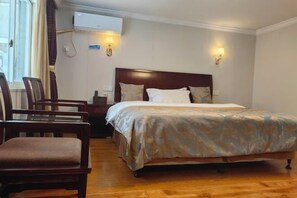 Habitación de hotel con una cama de madera, dos mesitas de noche, una silla y un equipo de aire acondicionado en la pared.